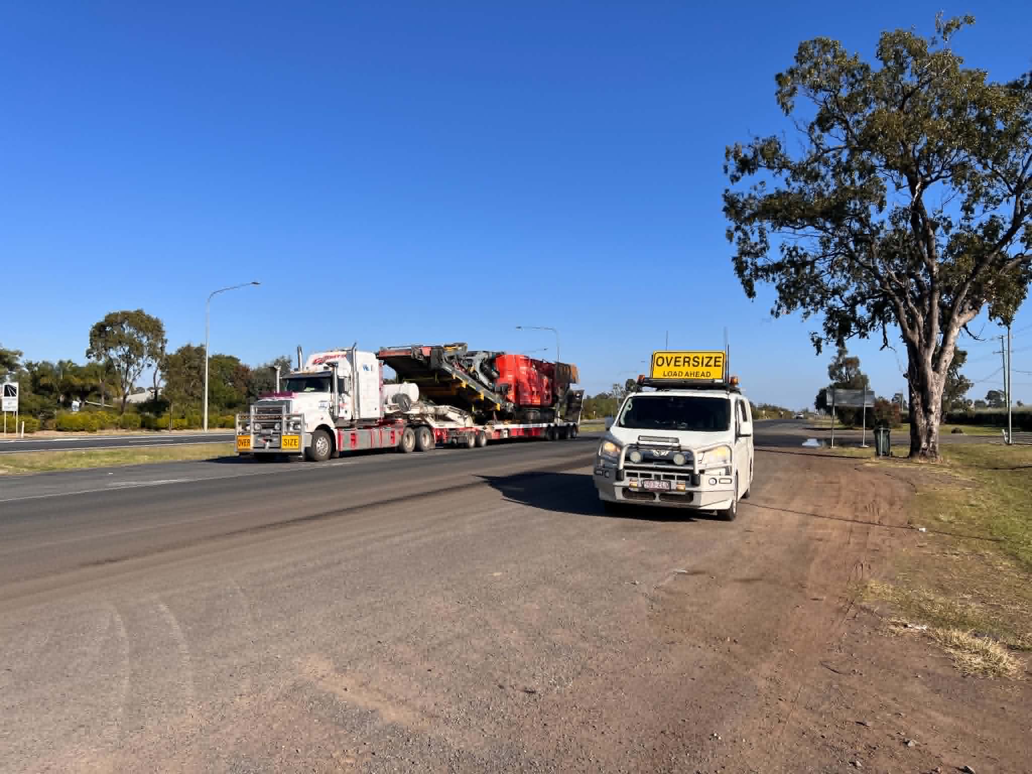 Oversize trucks and pilot vehicles staged on a remote Australian worksite at dusk